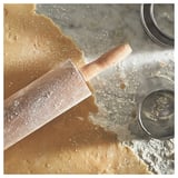 Rolling pin on floured gray counter with dough bits. Wood handle, metal rod. Part of MAGASIN baking set.