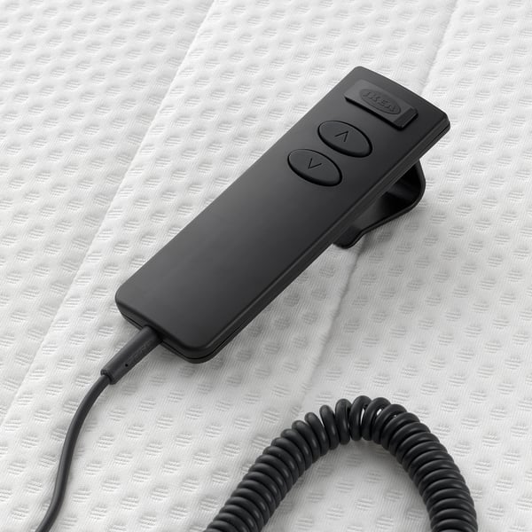 Black remote control for adjusting mattress angle, wired, on textured white bed.