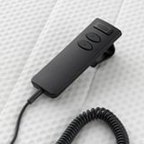 Black remote control for adjusting mattress angle, wired, on textured white bed.