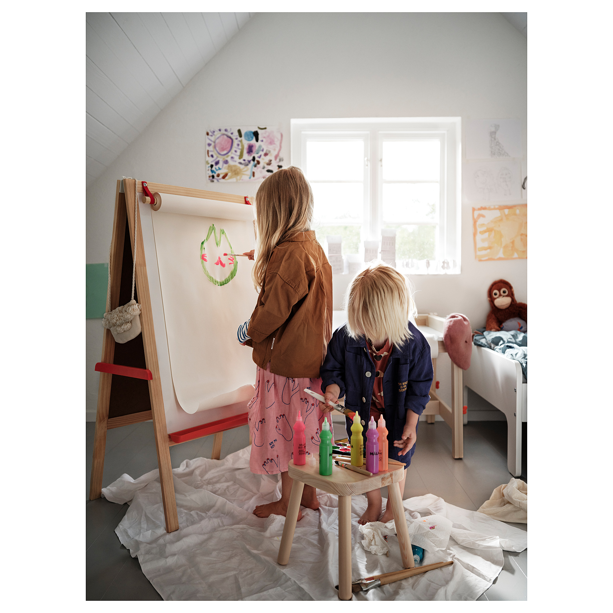 Kids drawing with markers at easel, window and toy monkey.