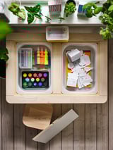 Wooden art supply drawers with colorful items and hanging plants.