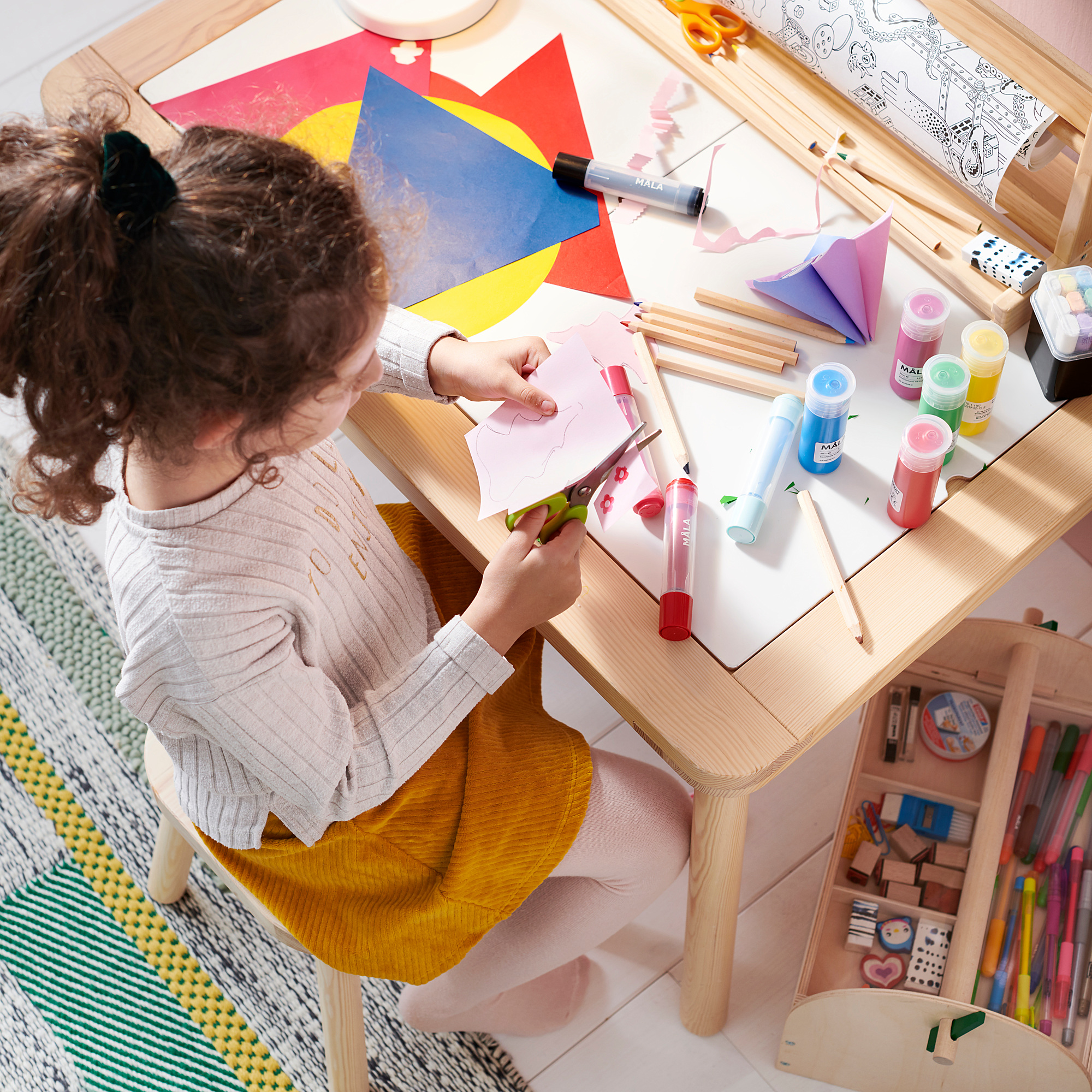 A child crafts with colorful paper and paint at a wooden table.