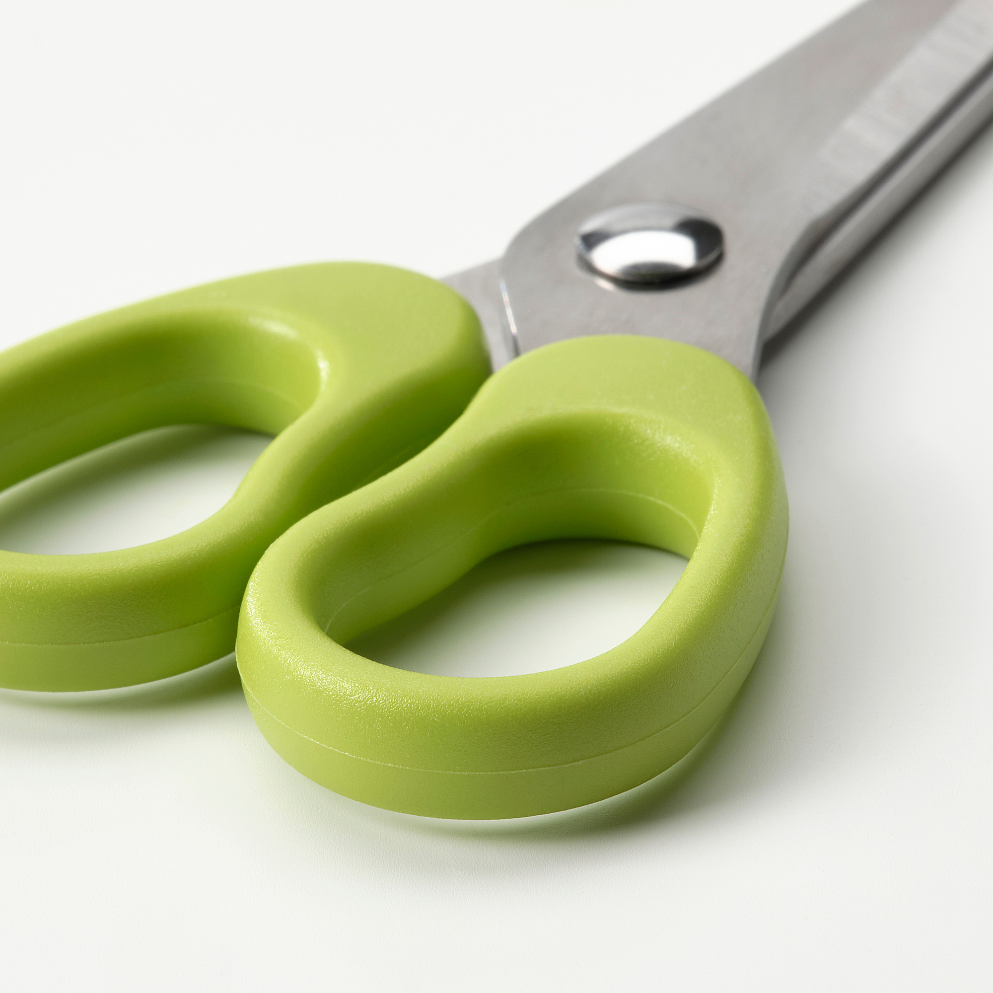 A pair of stainless steel scissors with bright green plastic handles, designed safely for children.