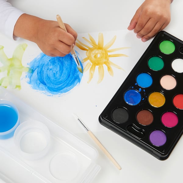 Childs hands paint with watercolors using brushes and palettes, creating vibrant art.