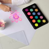Child painting a flower with neon watercolors from the MÅLA set, using a brush and a cup with water.