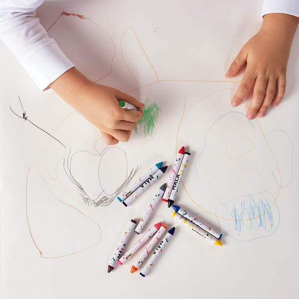 A child draws with colorful crayons on paper; six MÅLA crayons lie nearby.