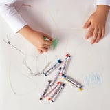 A child draws with colorful crayons on paper; six MÅLA crayons lie nearby.