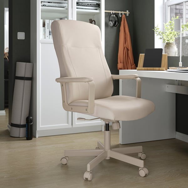 Modern home office setup with beige adjustable chair, light wooden floor, grey desk, orange blanket, and shelf with books.
