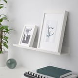 White wall shelf displaying two framed art pieces. Facilitates showcasing favorite items and art.