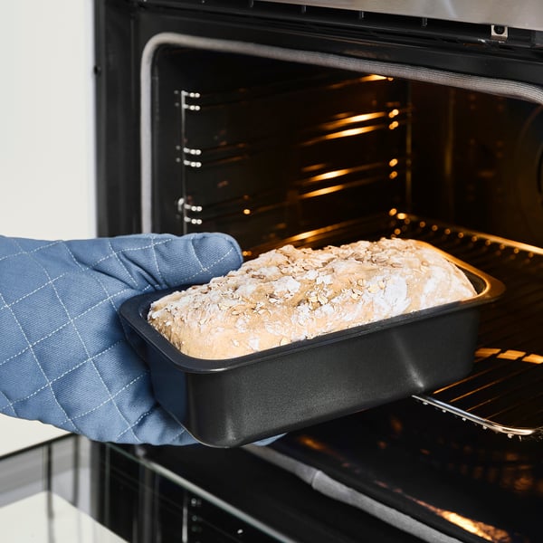 Holding bread pan in oven mitt.