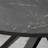 A close-up of a modern, round tabletop with a sleek, dark finish and subtle white veining patterns, supported by black metal legs.
