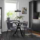 Modern dining setup with MARIEDAMM round table & grey chairs. Dark frames contrast light walls. Small size, centered under pendant light.