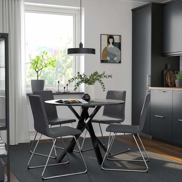 Modern dining set MARIEDAMM with round glass top table & grey fabric chairs, sleek metal legs, positioned near kitchen.