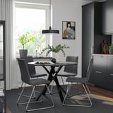 Modern dining set MARIEDAMM with round glass top table & grey fabric chairs, sleek metal legs, positioned near kitchen.