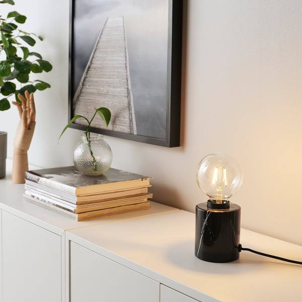 Modern decor: small black marble lamp on shelf, lit bulb, beside stacked books and vase.