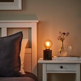 Cozy bedroom corner with small lamp & vase of flowers beside bed.