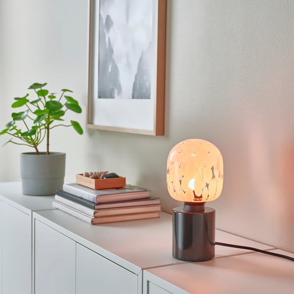 Decorative lamp on table, small, warm glow, near plant and books, black marble base.