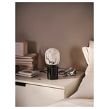 Modern bedroom with white bed, nightstand stocks books, & white marble lamp.