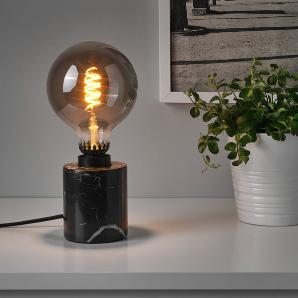 A table lamp with a black marble base and a glowing bulb, providing mood lighting.