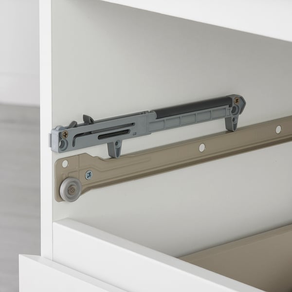 Close-up of soft-closing drawer mechanism; shows metallic slide, gray damper, and roller wheel on side of white cabinet.