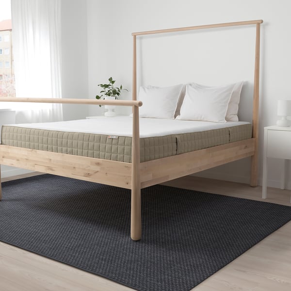 Light wood bed with white mattress, 2 pillows, plant. Central on gray rug, larger than nightstands.