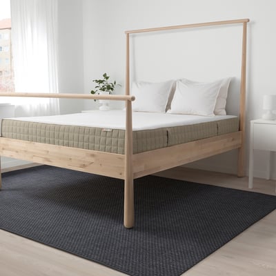 Light wood bed with white mattress, 2 pillows, plant. Central on gray rug, larger than nightstands.