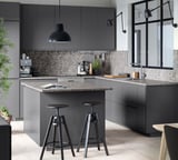 Modern grey kitchen with dark grey cabinets, marble countertops, black stools, and pendant lamp.
