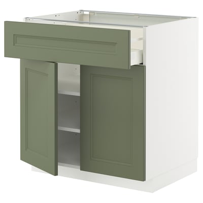 A METOD kitchen cabinet with green-gray doors and a white top. It a drawer and two shelves inside.