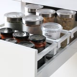 White kitchen drawer with multiple clear and metal-lidded jars, neatly organized with food items.