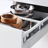 Open kitchen drawer with wooden and metal bowls, stainless tools.