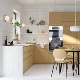 Modern kitchen with light wood cabinets, white marble countertop, stainless steel appliances, and a dining table with wooden chairs.