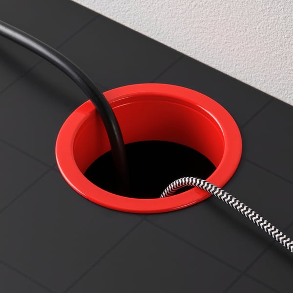 Red cable management grommet on black surface with coiled black and white cord.