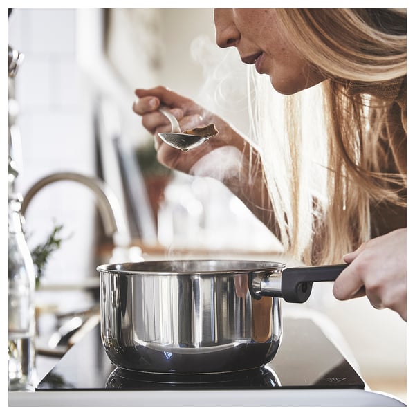 Woman cooking on black stove with MIDDAGSMAT saucepan.