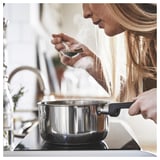 Woman cooking on black stove with MIDDAGSMAT saucepan.