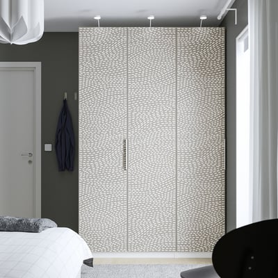 A large white wavy-patterned MISTUDDEN wardrobe, towering over a bed and chair, with its size dominating the room.