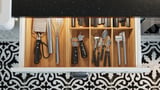 Kitchen drawer with wood divider holding black-handled utensils and knives.