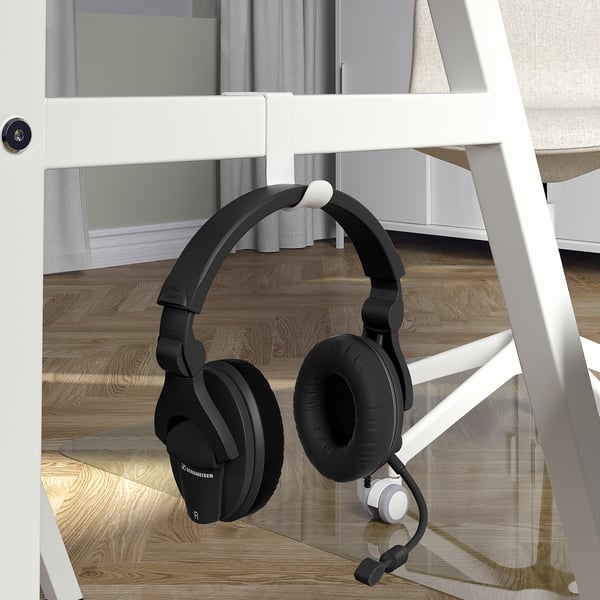 A black headset with microphone hangs on a white desks side hook.
