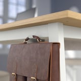 Brown leather bag hangs on wooden and metal shelf.