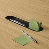 Black table slot with pen tray and notepad holder. Green sticky notes and pen nearby.