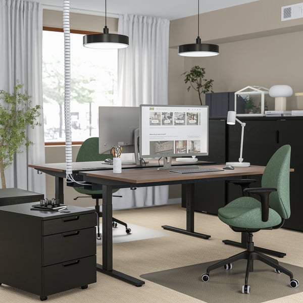 Modern home office with MITTZON desks, green chairs, and black cabinet. High-tech setup with large monitors and minimalist design.