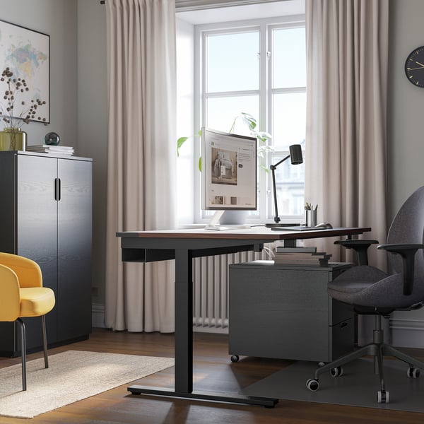 Modern home office with MITTZON black height-adjustable desk, gray chair, large monitor, and yellow accent chair. Wide window with light curtains.