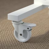 Close-up of a sturdy, white office castor with lock and spherical wheel on beige carpet.