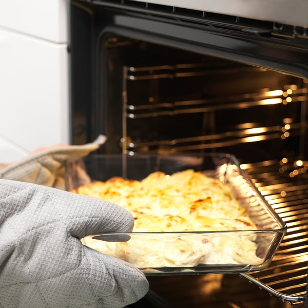 Person wearing an oven mitt holding a glass dish of baked food, taking it out of the oven.