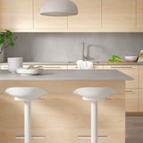 White MÖCKLARP stools under light gray kitchen island with plates, bowls, and napkins. Pendant light overhead in modern kitchen.