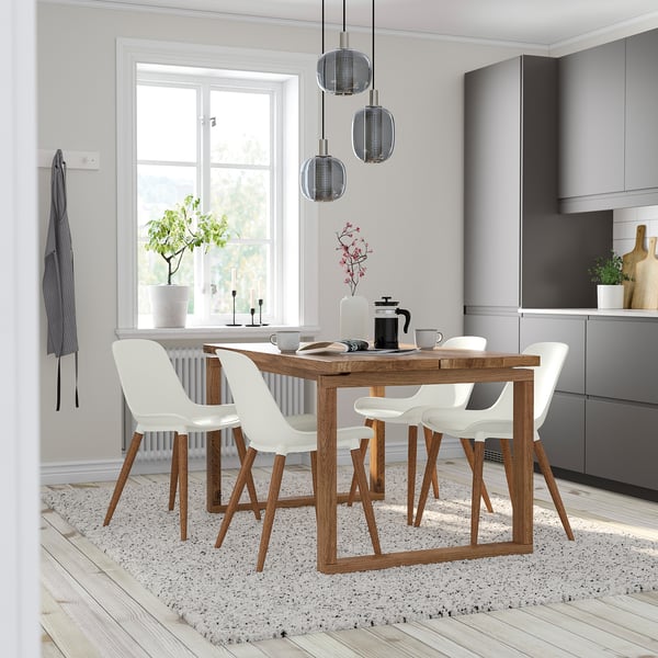 Modern dining set with oak table, four white chairs, stylish pendant lights, and a grey rug, creating a cozy kitchen nook.