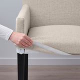 A hand adjusts a removable, machine-washable cover on a beige MÖRBYLÅNGA chair with black metal legs.
