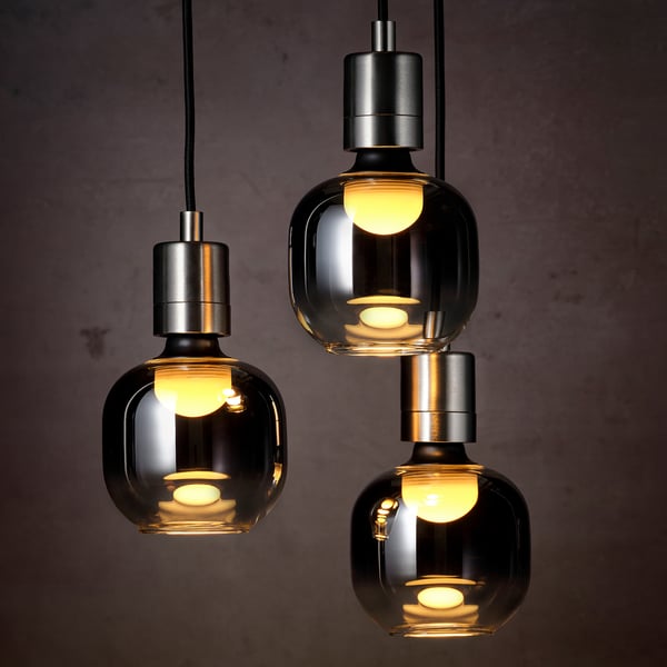 Three smoky grey glass pendants hang, each lit warmly, casting a cozy glow. Led lighting within adds modern elegance.