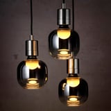 Three smoky grey glass pendants hang, each lit warmly, casting a cozy glow. Led lighting within adds modern elegance.