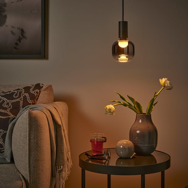 Cozy corner with beige couch, MOLNART light, flowers, mug, sphere, soft warm glow.