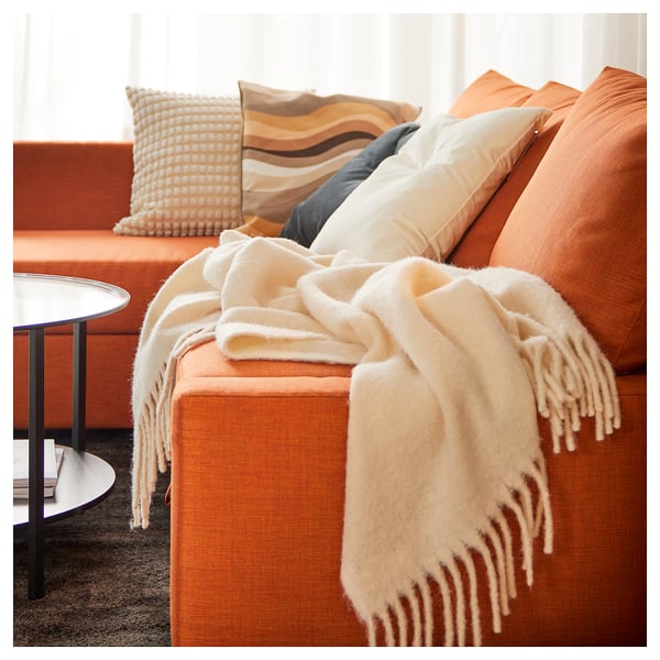 Orange couch, beige blanket, colorful pillows, side table